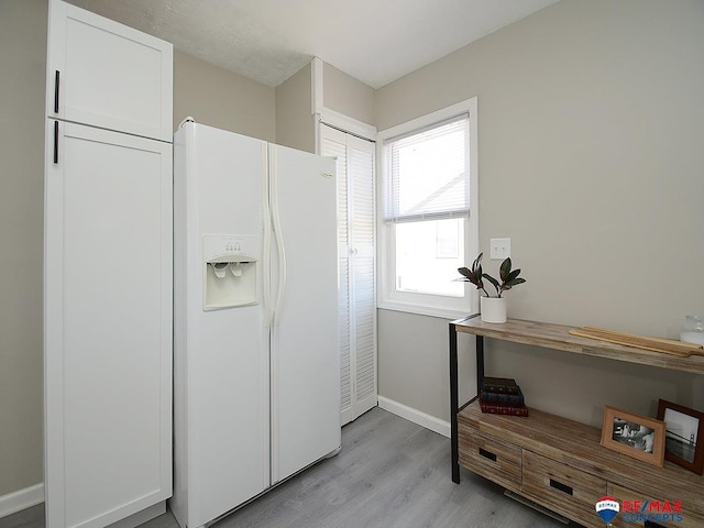 interior space with white cabinetry, white refrigerator with ice dispenser, and light hardwood / wood-style flooring