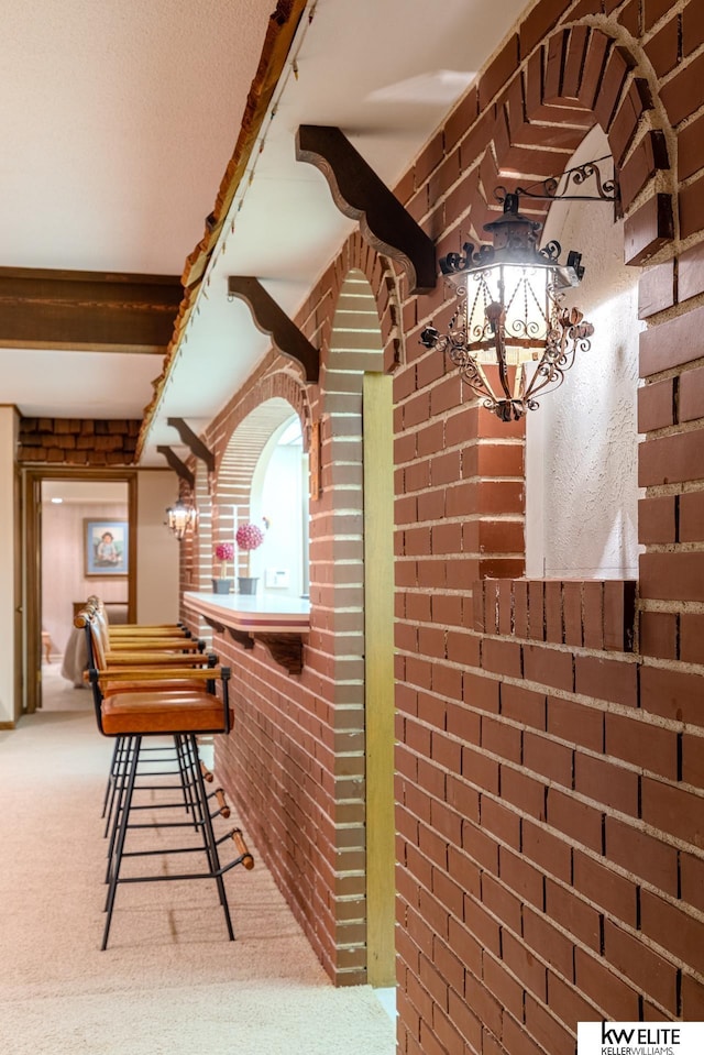 interior space with brick wall, beamed ceiling, and carpet flooring