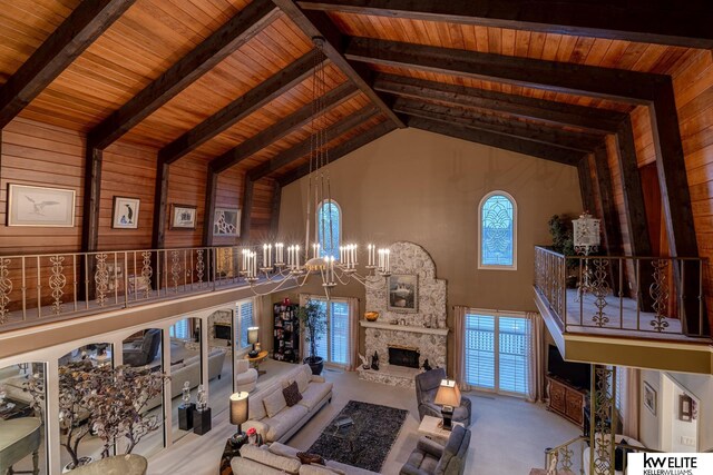 living room featuring a notable chandelier, wood walls, beamed ceiling, a stone fireplace, and high vaulted ceiling