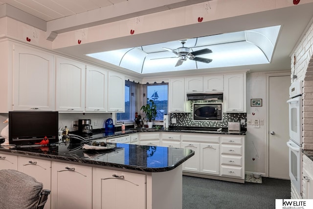 kitchen with kitchen peninsula, ceiling fan, dark stone counters, white cabinets, and black appliances