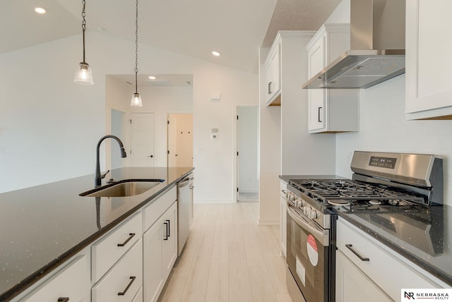 kitchen featuring pendant lighting, lofted ceiling, wall chimney range hood, stainless steel appliances, and sink