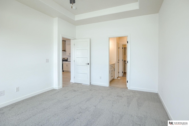 unfurnished bedroom with a tray ceiling, ensuite bathroom, and light carpet