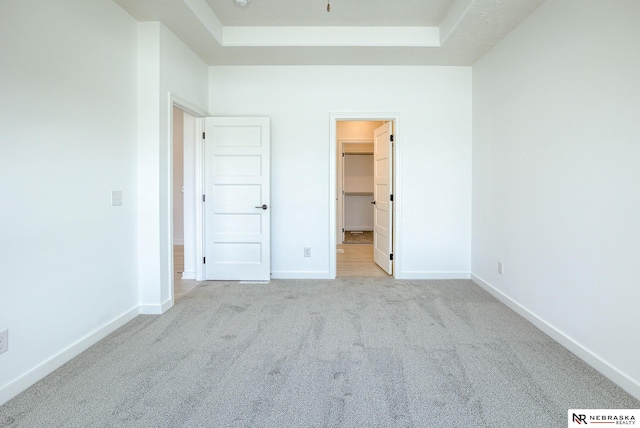 unfurnished bedroom featuring light carpet, a walk in closet, a closet, and a raised ceiling