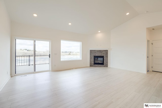 unfurnished living room featuring vaulted ceiling, a stone fireplace, and light hardwood / wood-style flooring