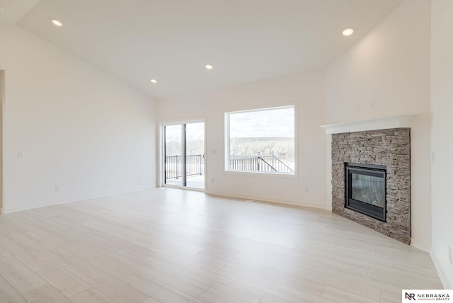 unfurnished living room with lofted ceiling, light hardwood / wood-style flooring, and a stone fireplace