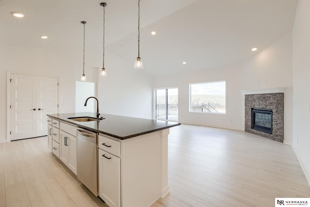 kitchen with a stone fireplace, an island with sink, dishwasher, white cabinets, and sink