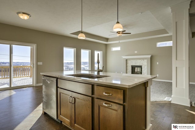 kitchen with dishwasher, dark hardwood / wood-style floors, an island with sink, a stone fireplace, and a raised ceiling