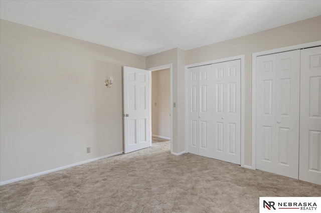 unfurnished bedroom featuring multiple closets and light colored carpet