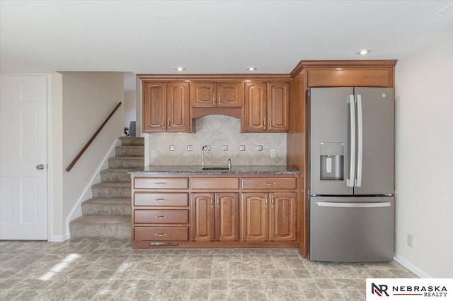 kitchen with stainless steel refrigerator with ice dispenser, sink, backsplash, and dark stone counters