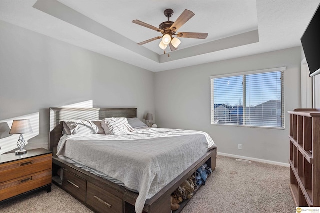 carpeted bedroom with ceiling fan and a tray ceiling