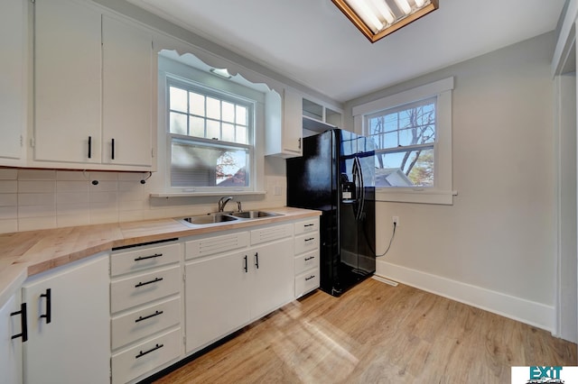 kitchen featuring white cabinetry, light hardwood / wood-style floors, decorative backsplash, black refrigerator with ice dispenser, and sink