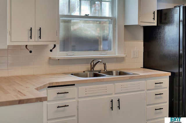 kitchen with white cabinets, butcher block counters, sink, backsplash, and black fridge