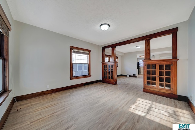 unfurnished room featuring light wood-type flooring, a textured ceiling, and decorative columns