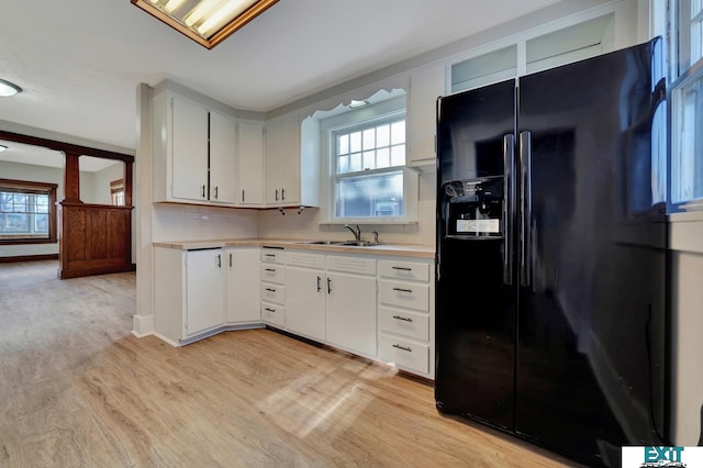 kitchen featuring black fridge, a wealth of natural light, sink, white cabinetry, and light wood-type flooring