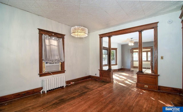 empty room with wood-type flooring, ceiling fan with notable chandelier, radiator heating unit, and decorative columns