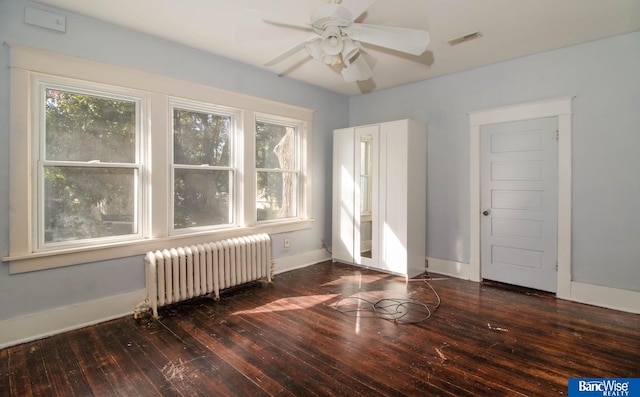 empty room featuring ceiling fan, dark wood-type flooring, a wealth of natural light, and radiator heating unit