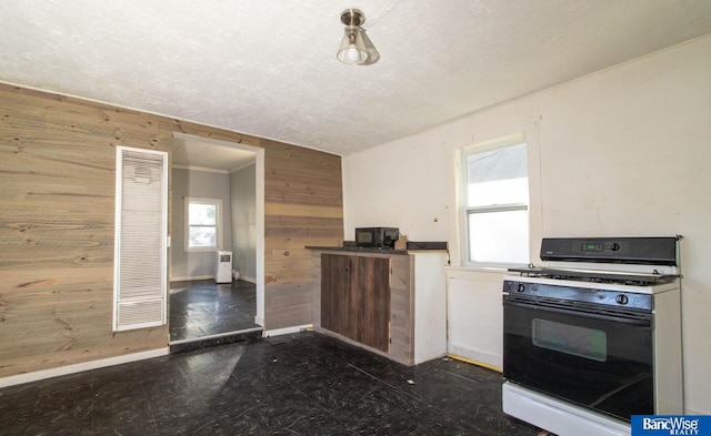 kitchen featuring a textured ceiling, white gas range, and wooden walls