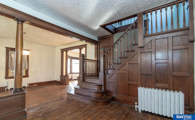 staircase featuring decorative columns, hardwood / wood-style flooring, and radiator heating unit