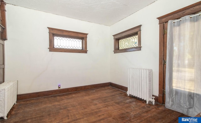 unfurnished room featuring radiator heating unit and dark hardwood / wood-style flooring