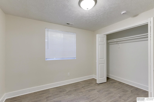 unfurnished bedroom with wood-type flooring, a closet, and a textured ceiling