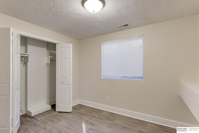 unfurnished bedroom featuring wood-type flooring, a closet, and a textured ceiling