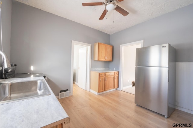 kitchen featuring ceiling fan, sink, light wood-type flooring, a textured ceiling, and stainless steel fridge