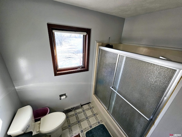 bathroom featuring toilet, a shower with door, and a textured ceiling