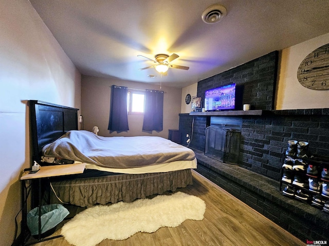 bedroom with hardwood / wood-style floors, a fireplace, and ceiling fan