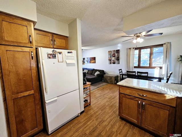 kitchen featuring ceiling fan, wood-type flooring, light stone countertops, a textured ceiling, and white refrigerator