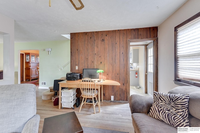 office area featuring ceiling fan, light hardwood / wood-style flooring, and wooden walls