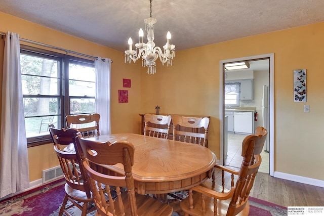 dining space with a textured ceiling, hardwood / wood-style floors, and a chandelier