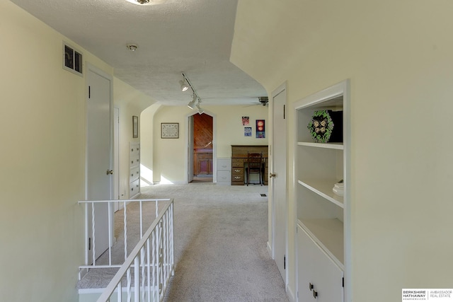 hall with light colored carpet, a textured ceiling, and rail lighting