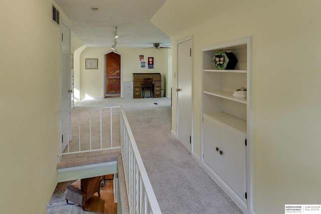 hallway featuring light colored carpet and built in features