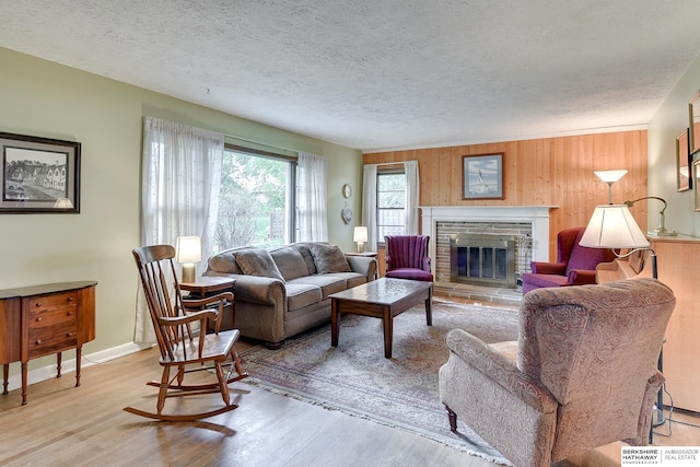 living room featuring a stone fireplace, wooden walls, a textured ceiling, and light hardwood / wood-style flooring