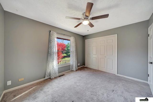 unfurnished bedroom with a textured ceiling, ceiling fan, a closet, and light colored carpet