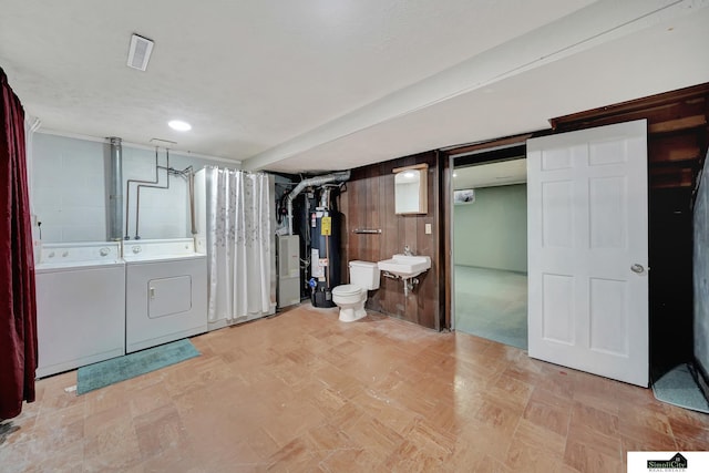 basement with washing machine and dryer, sink, wood walls, and gas water heater