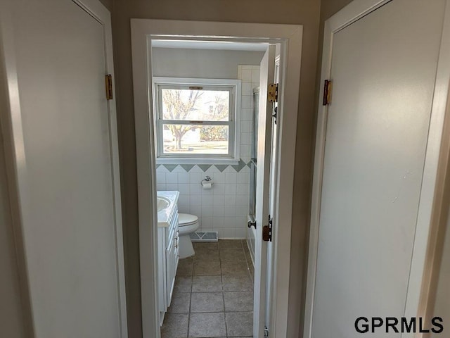 bathroom with toilet, tile patterned flooring, tile walls, and vanity