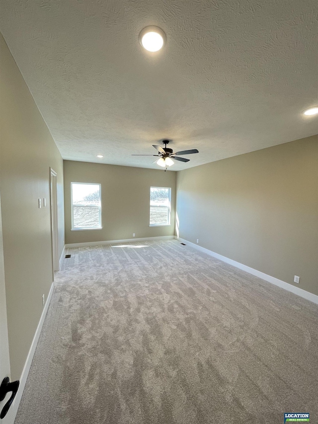 carpeted spare room featuring a textured ceiling, baseboards, and a ceiling fan