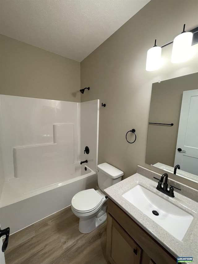 full bath with shower / bath combination, toilet, wood finished floors, a textured ceiling, and vanity