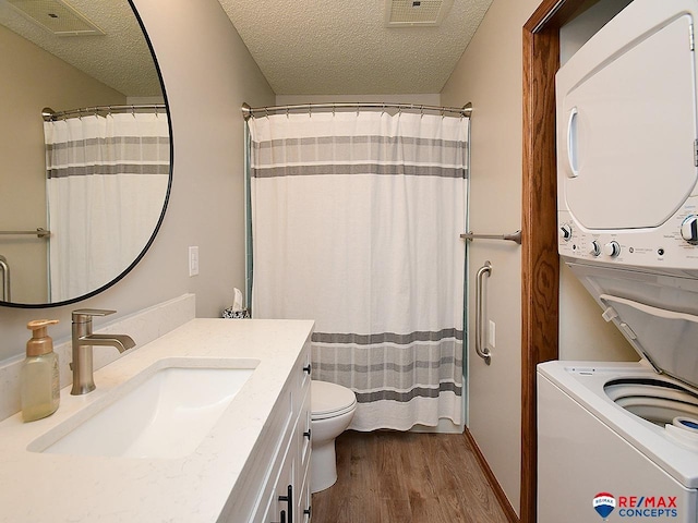 bathroom featuring stacked washer / dryer, a textured ceiling, vanity, toilet, and hardwood / wood-style flooring