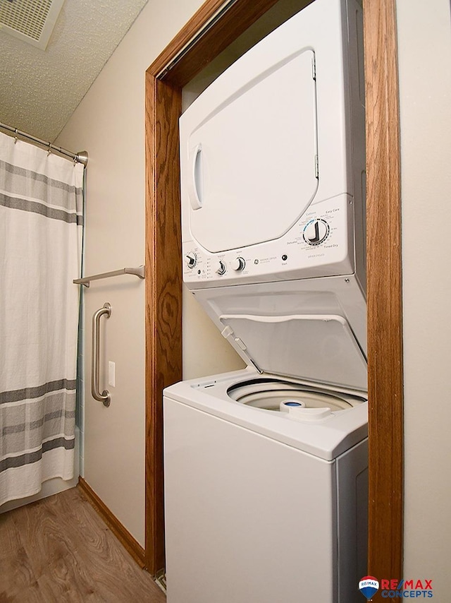 laundry room featuring wood-type flooring, a textured ceiling, and stacked washer / drying machine