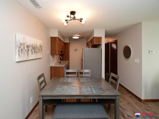 dining room with a textured ceiling, a chandelier, wood-type flooring, and sink