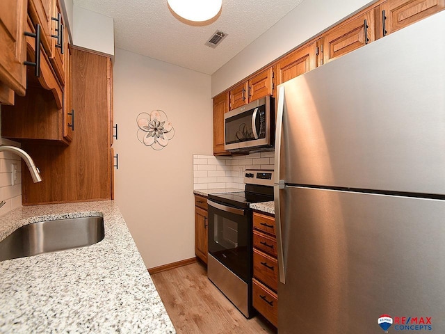 kitchen featuring light hardwood / wood-style floors, stainless steel appliances, decorative backsplash, a textured ceiling, and sink