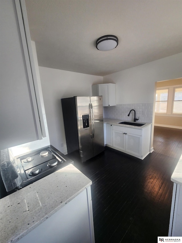 kitchen featuring sink, stainless steel fridge, white cabinetry, light stone countertops, and decorative backsplash