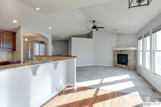 kitchen with vaulted ceiling, a kitchen breakfast bar, kitchen peninsula, ceiling fan, and a fireplace