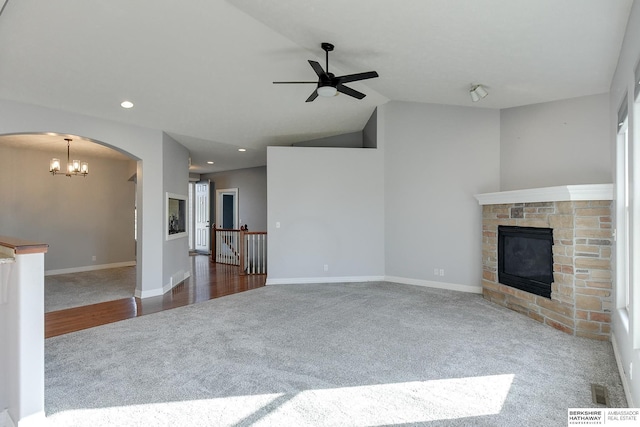 unfurnished living room featuring carpet flooring, lofted ceiling, a stone fireplace, and ceiling fan with notable chandelier