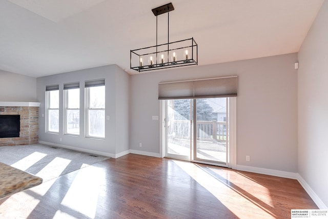 unfurnished living room with a stone fireplace, light hardwood / wood-style flooring, and a chandelier