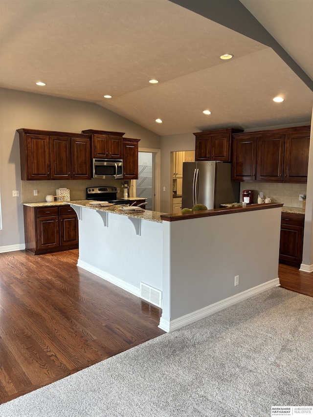 kitchen featuring lofted ceiling, a breakfast bar area, appliances with stainless steel finishes, dark brown cabinets, and a kitchen island