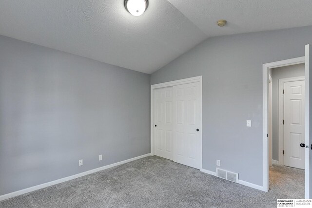 unfurnished bedroom with vaulted ceiling, light carpet, a textured ceiling, and a closet