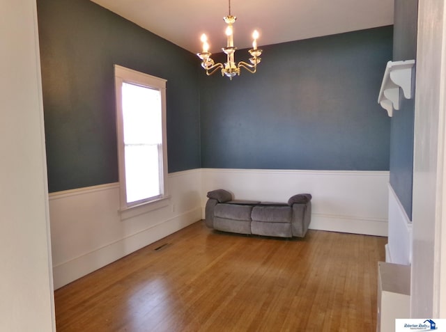 unfurnished room featuring a wainscoted wall, wood finished floors, and a chandelier